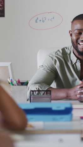 video of happy african american male teacher sitting at desk during math lesson