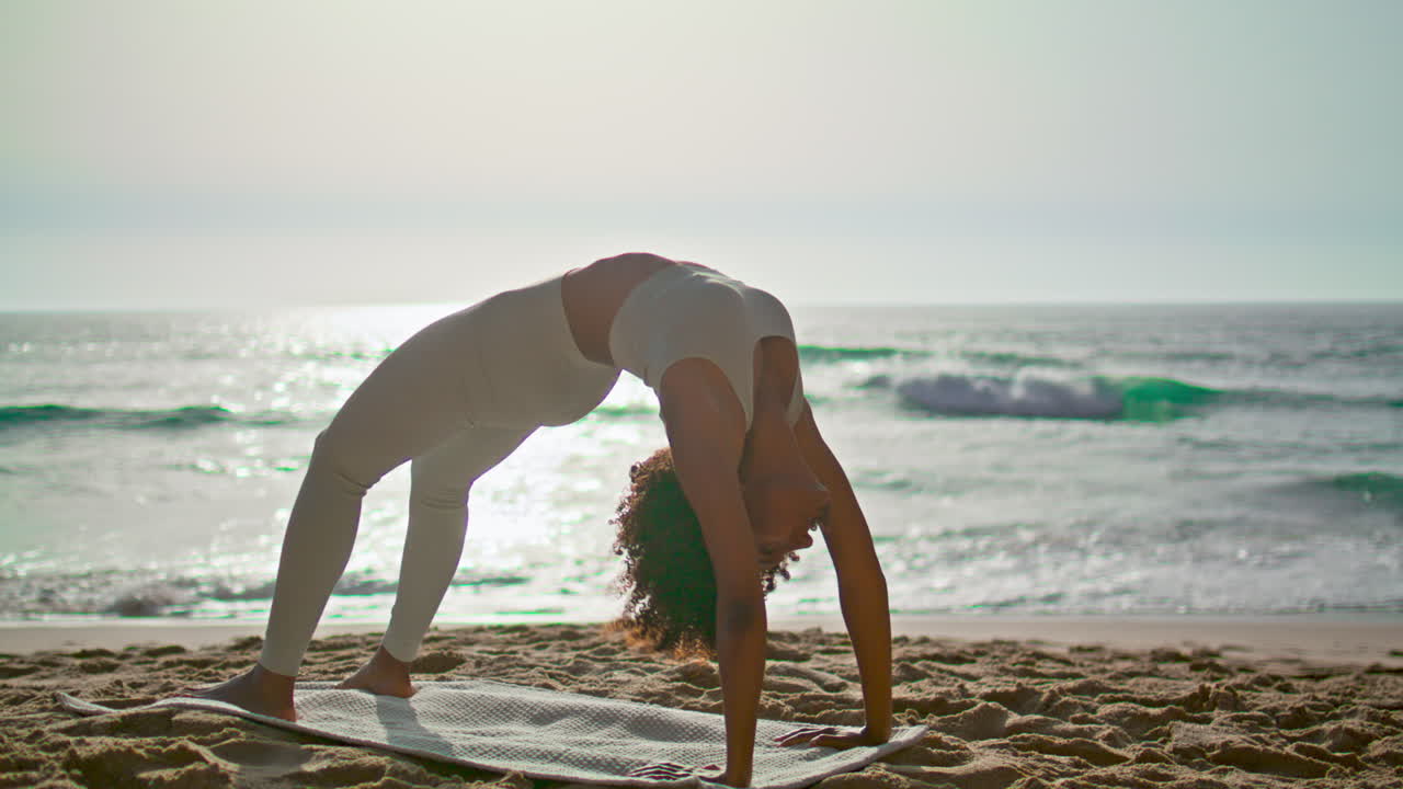 Woman practicing Urdhva Dhanurasana on sand beach at sunrise. Girl training yoga