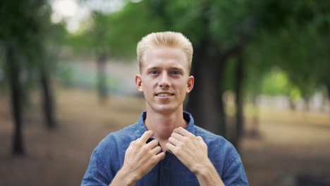 Close-up-portrait-young-happy-blond-man-standing-in-nature-between-park-trees-relaxes,-breathes-fresh-air.-Male-enjoys-a-life-of