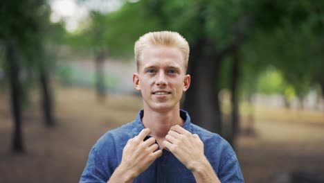 close up portrait young happy blond man standing in nature between park trees relaxes, breathes fresh air. male enjoys a life of