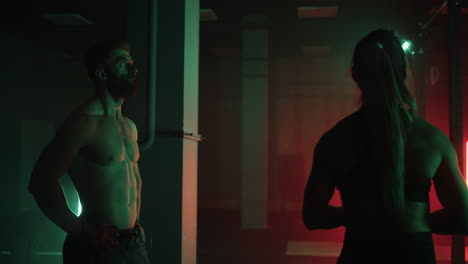 two men and a woman in the gym do pull-ups on the horizontal bar together in a dark neon light. atmosphere of fitness and training