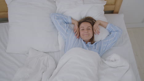 mujer hermosa feliz se despierta sonriendo y estirando los brazos en su cama en el dormitorio. mujer joven utiliza el tiempo de relajación en casa. estilo de vida mujer en el concepto de casa.