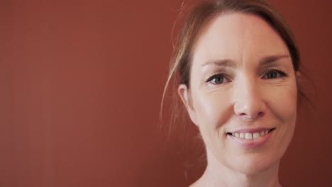 Caucasian-mid-adult-woman-smiling-at-camera-against-brown-wall-in-yoga-studio