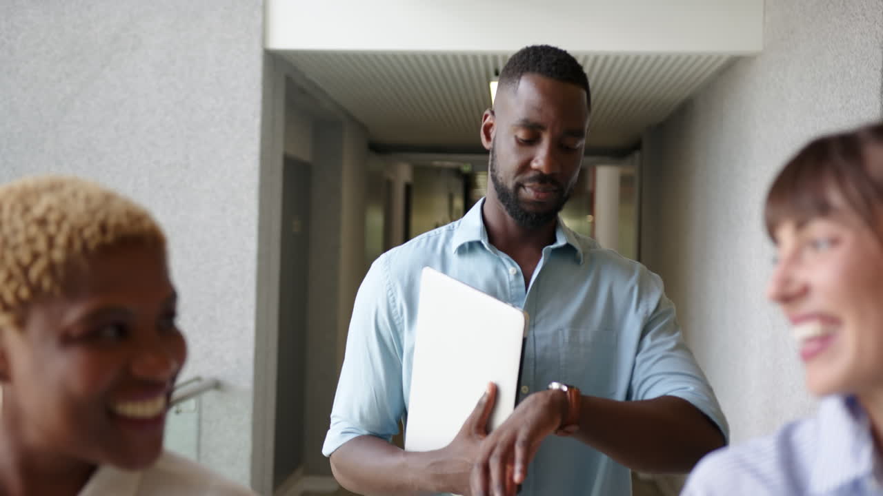 Checking time, african american man with laptop and smiling with multiracial colleagues, at office