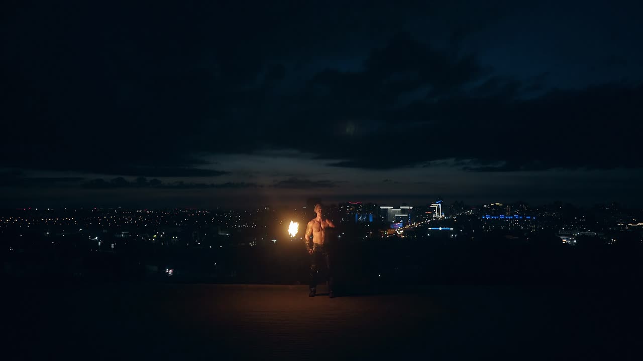 молодой блондин делает огненное шоу посреди ночи вращается горящий факел выдыхает огонь делает огненный шар