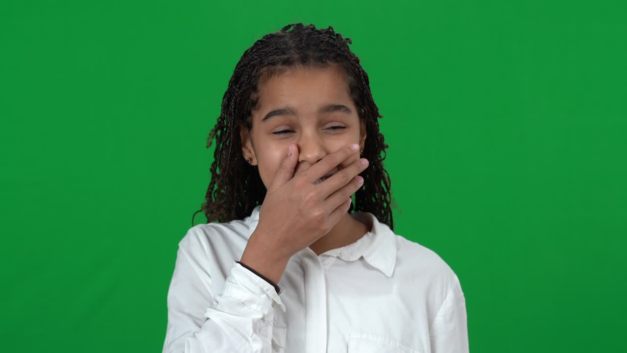 Close-up portrait of bored teenage African American girl yawning on green screen. Beautiful teenager looking at camera at chromakey background. Boredom and tiredness concept.