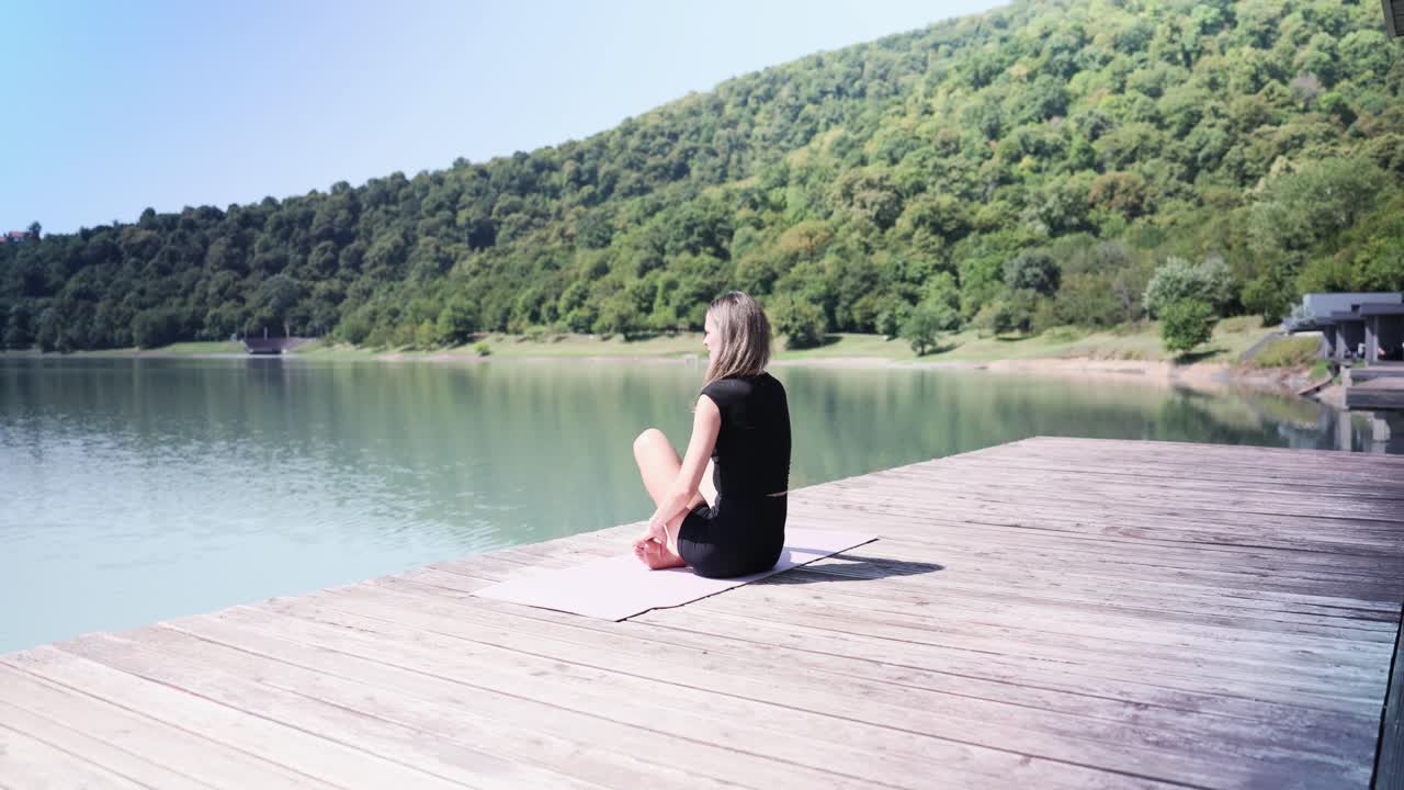 Woman practicing yoga on a dock by a lake