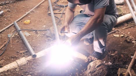 Professional-welder-employing-industrial-welding-machine-to-put-together-two-pieces-of-metal-creating-a-metalic-structure-as-part-of-his-daily-work-at-a-local-small-business