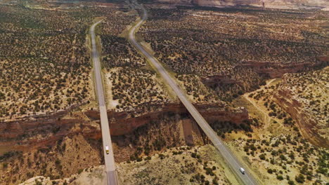 huge ditch in the deserted lands of utah national park. two bridges connecting the edges of trench with cars moving by. aerial view.