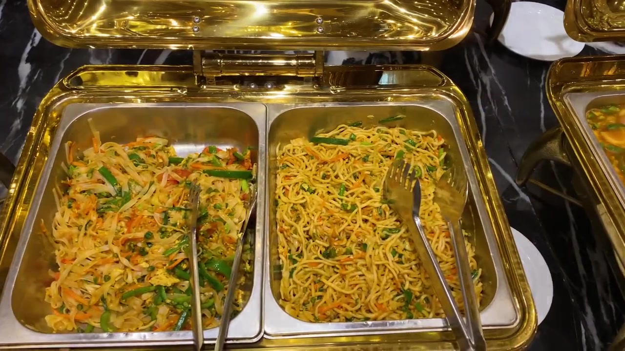 Noodles chow mein con verdure saltate in padella e pollo serviti in uno scaldavivande dorato a buffet - ripresa panoramica