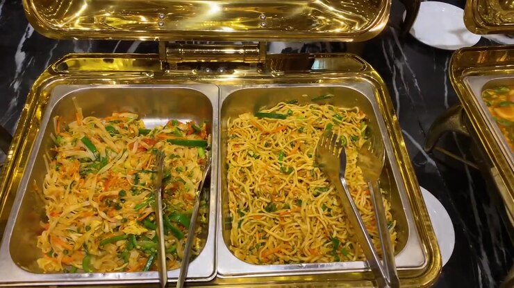 Chow mein nudler med grøntsags-wok og kylling serveret i gylden varmeskål ved buffet - panorering