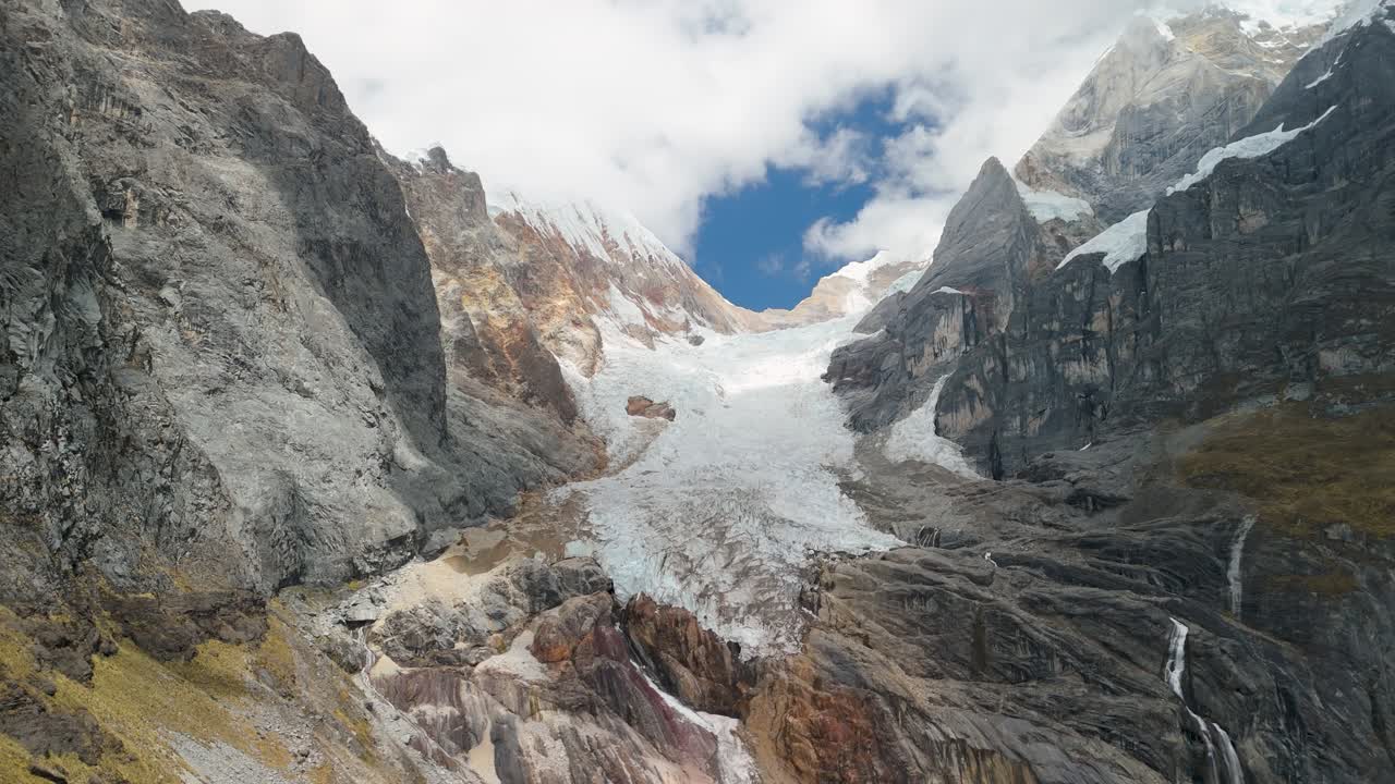 A slow push-in aerial shot moves towards a massive mountain glacier, revealing the details of the ice and rugged rock faces in the remote Huayhuash Andes of Peru