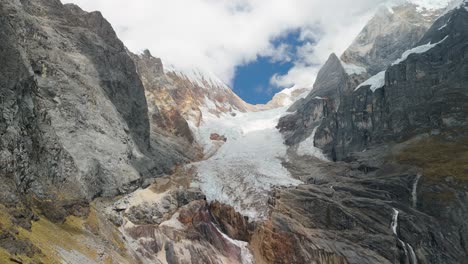 a slow push-in aerial shot moves towards a massive mountain glacier, revealing the details of the ice and rugged rock faces in the remote huayhuash andes of peru