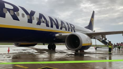 passengers board an aircraft under grey, rainy skies, stepping carefully as raindrops fall, reflecting on the wet tarmac, adding a calm yet rushed atmosphere.