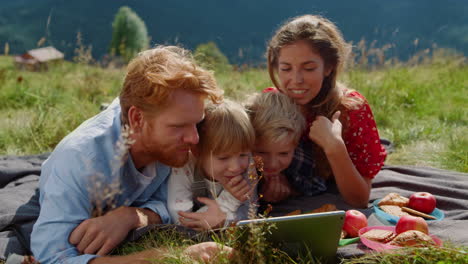 family looking tablet screen lying green meadow close up. parents kids relaxing.