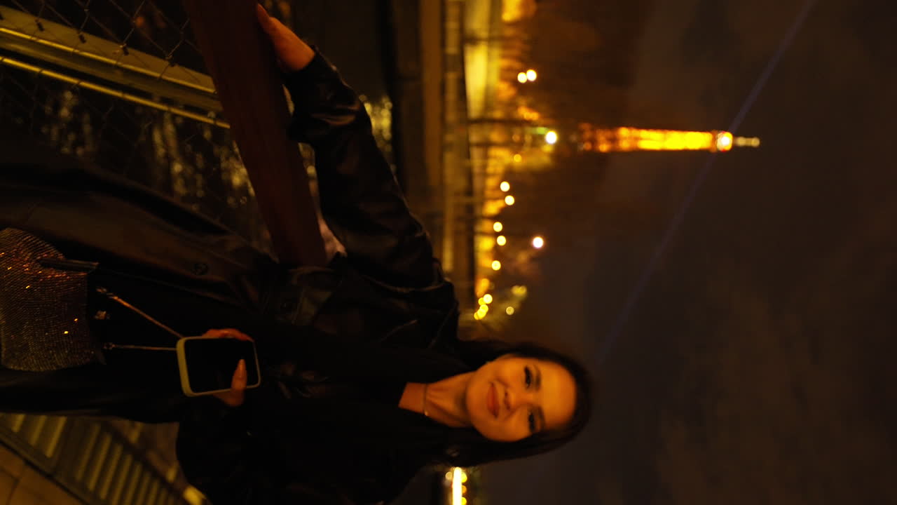 video vertical de una hermosa joven en un barco en el río sena en parís, con el tour eiffel en el fondo, por la noche, francia