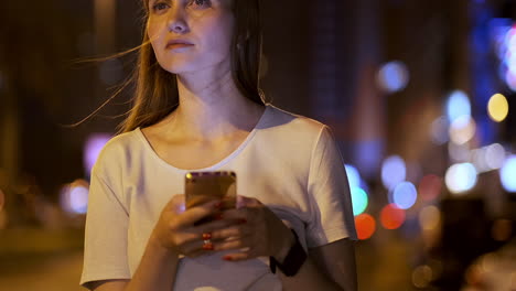 a young woman at night in the city calls a taxi through a smartphone while looking into the screen of a mobile phone and pointing out the coordinates and address of the trip.