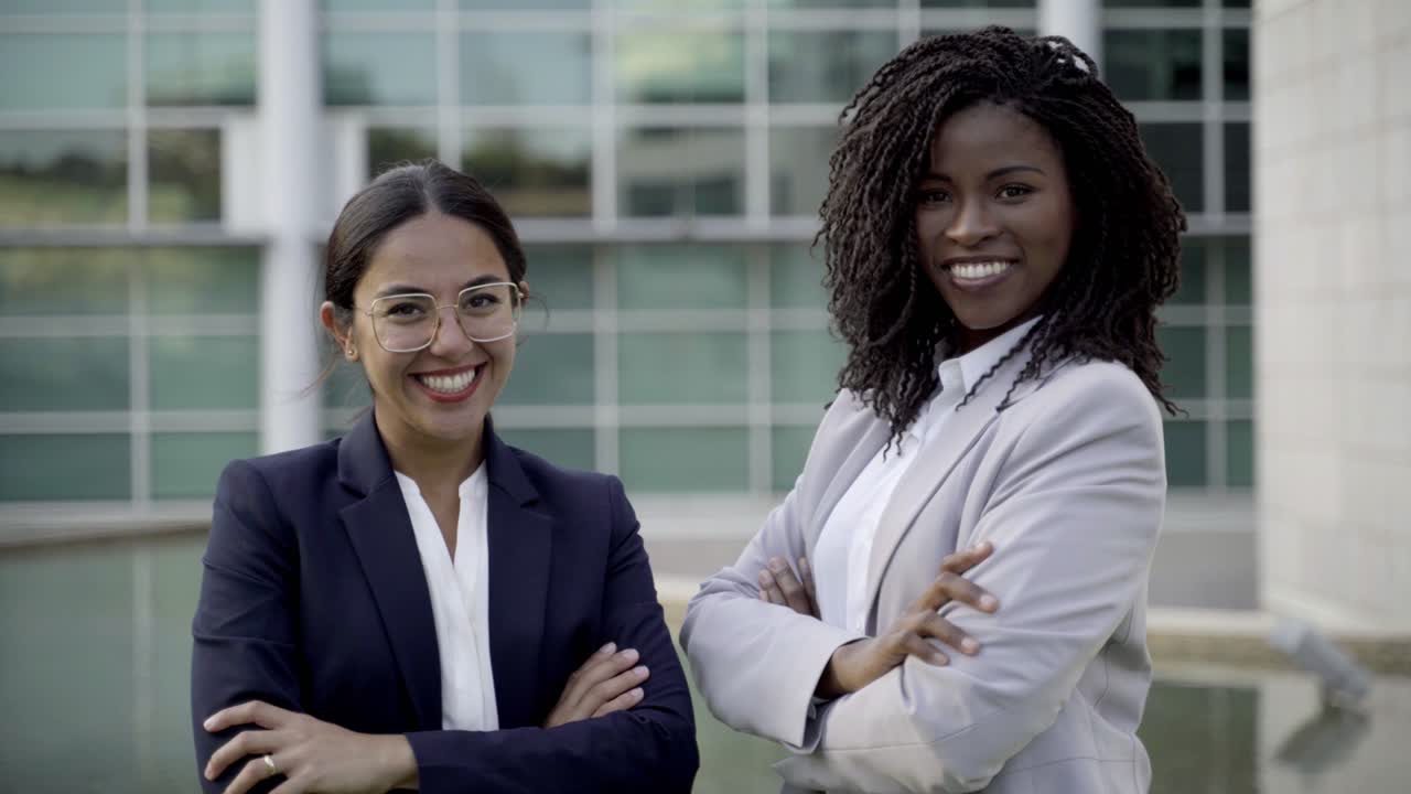 dos colegas sonrientes de pie con los brazos cruzados en la calle