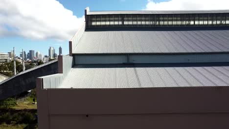 Slowly-panning-across-the-rooftop-of-an-abandoned,-disused,-derelict-Power-Station-Warehouse-Factory-in-East-Perth-with-a-view-to-the-Perth-skyline-behind