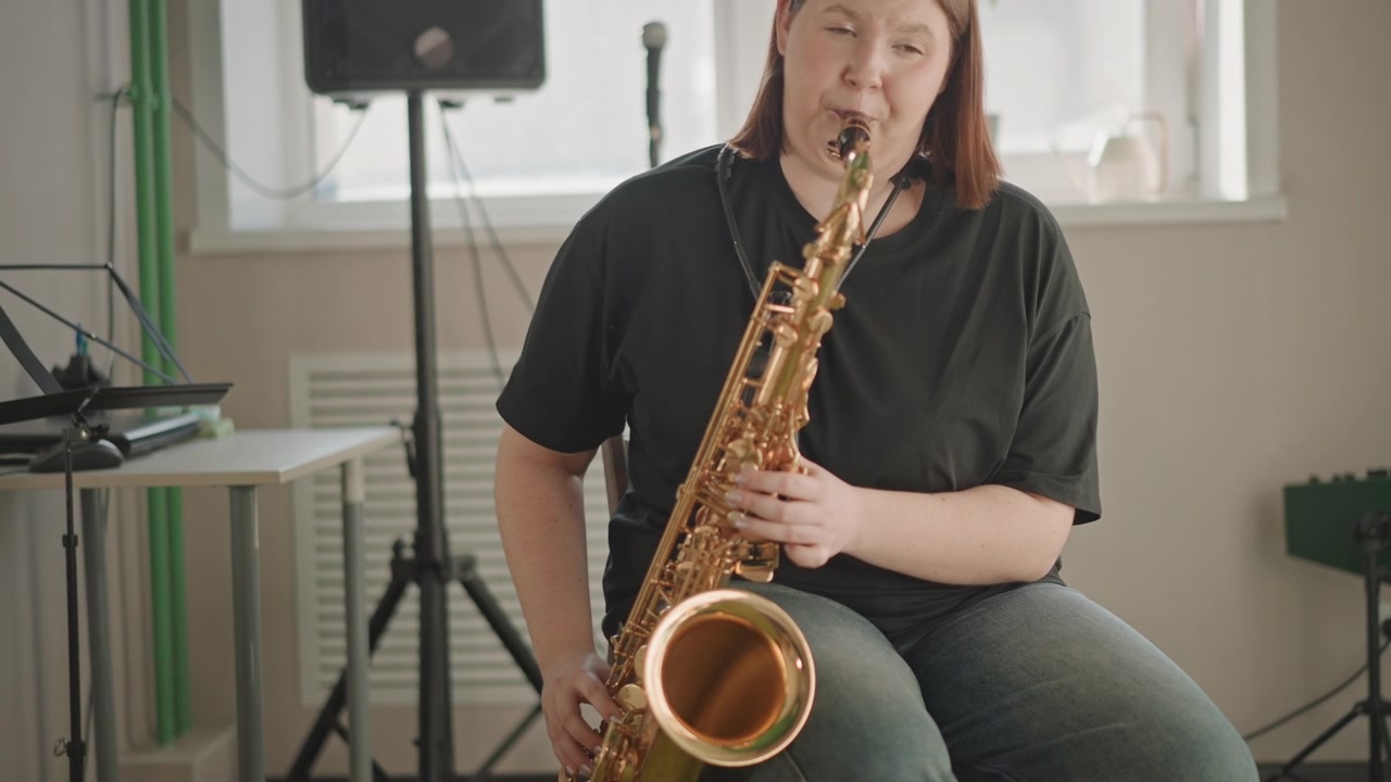 Primo piano su gamba e campana di un sassofonista durante una sessione di insegnamento, focus sul battito del piede e sulla postura sullo sgabello, amplificatore e microfono sullo sfondo, atmosfera educativa amichevole, luce mattutina