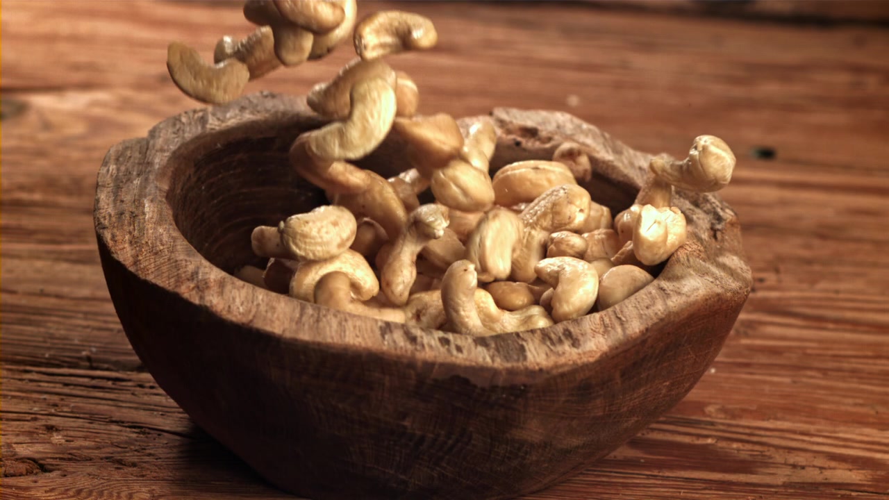 Cashewnøtter faller ned i en rustikk treskål i sakte film