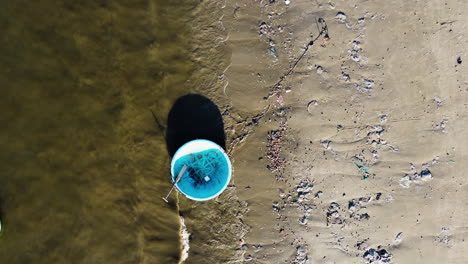 floating disposable plactic bags and rice boats rippling on the slowly rooling waves on the polluted beach while a dogs and his owner are walking in vietnam