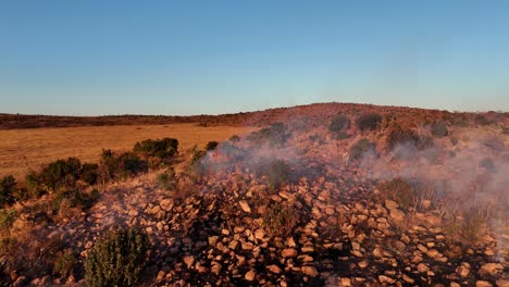 empleados de la granja terminan de apagar un incendio con batedores de fuego en una colina rocosa en el campo de áfrica