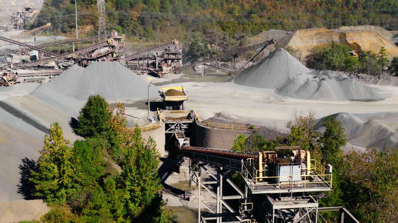 Quarry processing facility and gravel piles, dump truck loads hopper to transport into conveyor belt, aerial medium