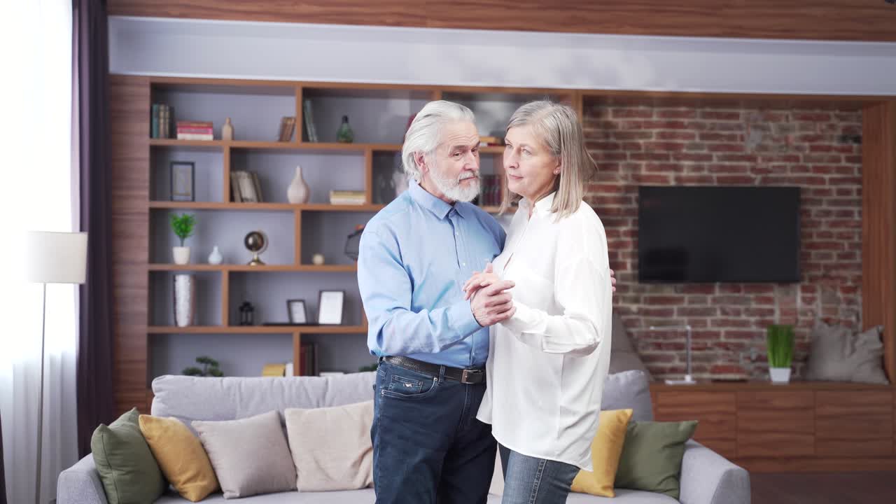 senior elderly romantic couple in love dancing at home. Old gray haired family hug together. Husband and wife celebrate wedding anniversary while listen to music