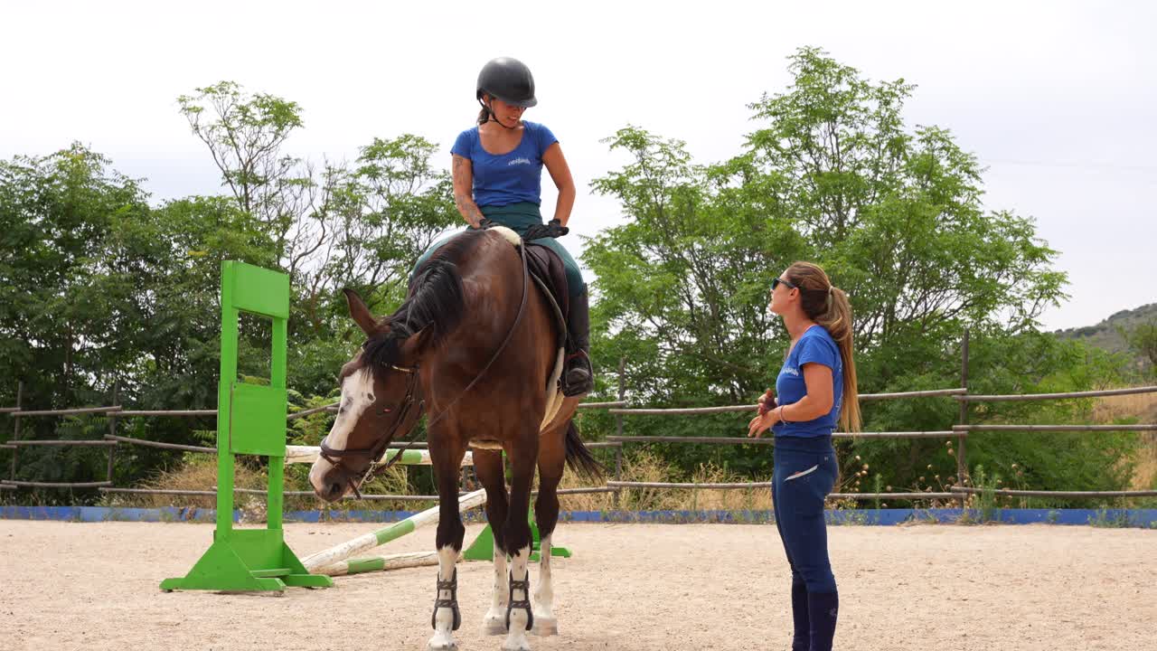 Jinete femenina a caballo se detiene frente a su entrenador para recibir orientación sobre cómo mejorar los saltos.