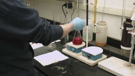 dolly shot of chemist running a lab experiment with colored liquid in a flask