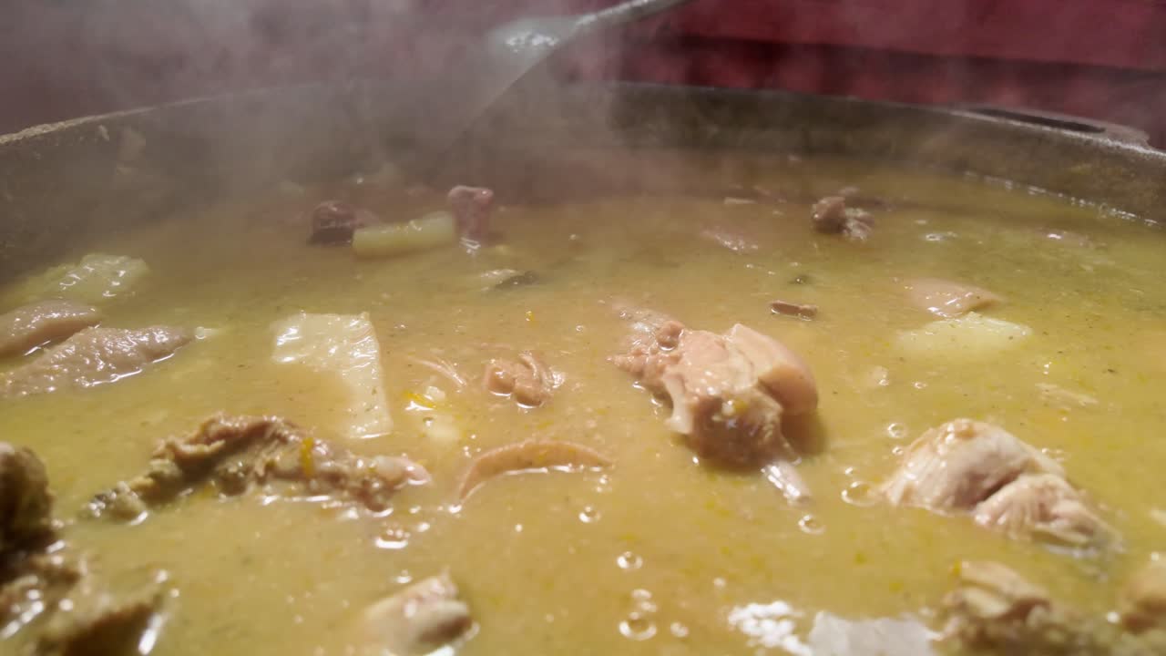 Primo piano di una pentola piena di Sancocho dominicano, mentre un cucchiaio di metallo mescola le carni e le verdure cotte, con il vapore che enfatizza il calore di questo piatto tradizionale