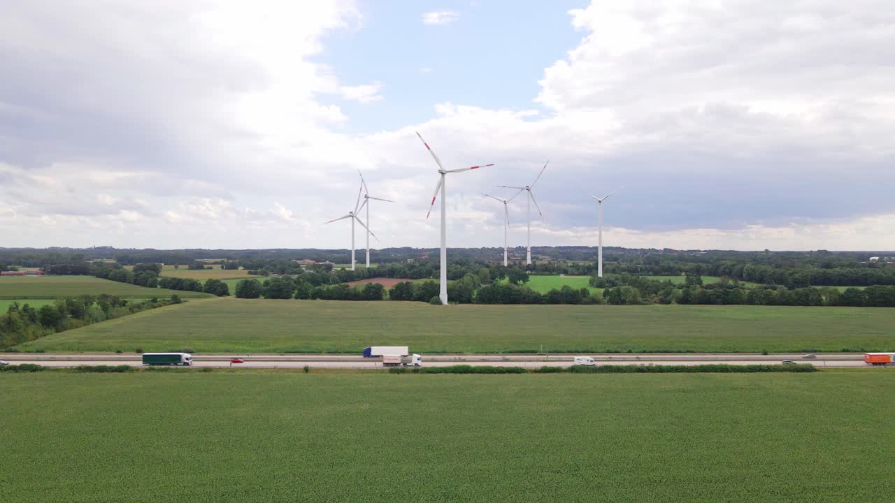 Drone footage of wind turbines beside a highway, surrounded by farmland and cornfields