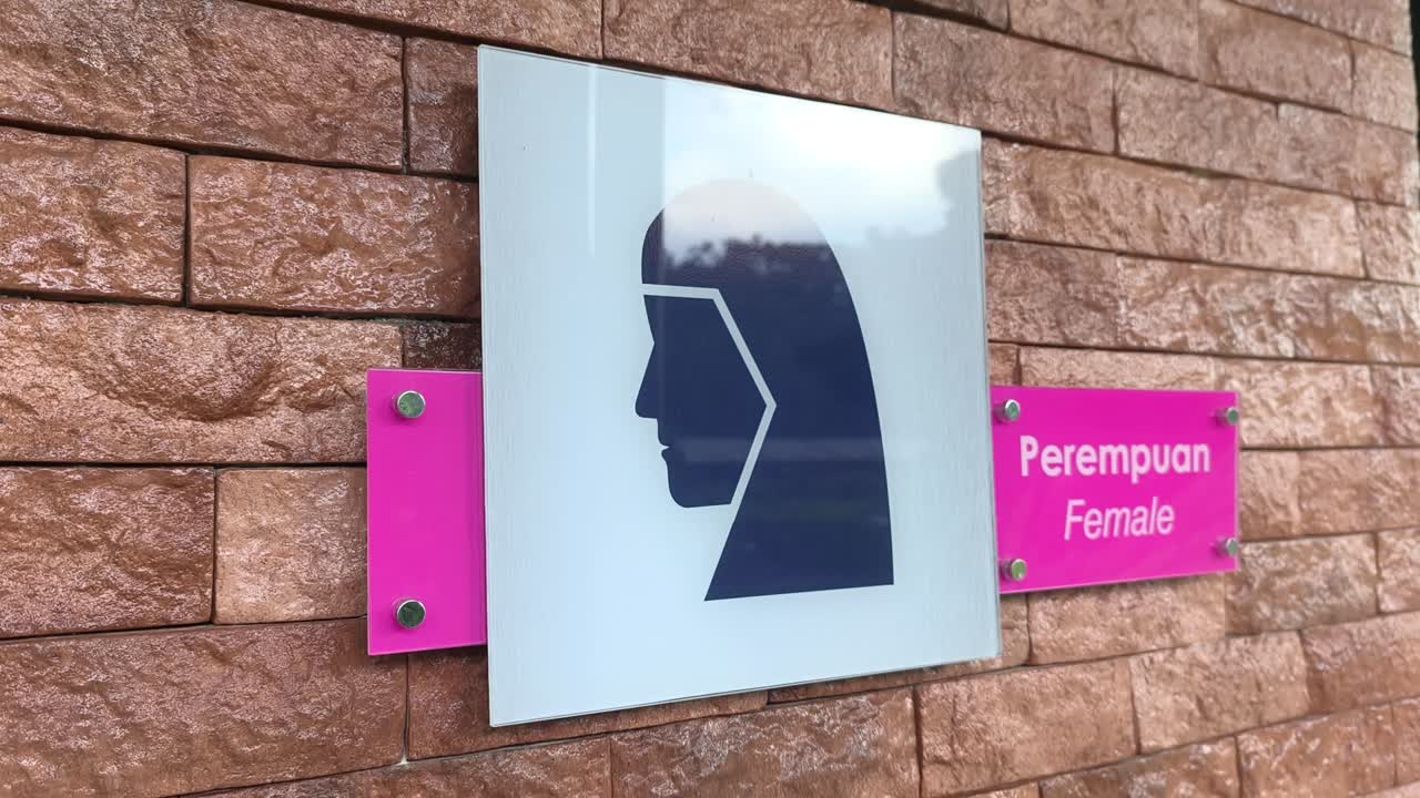 Papan tanda yang jelas untuk mushola umum terpasang di dinding. Papan tersebut menampilkan grafis pria atau wanita dengan teks dalam bahasa Melayu dan Inggris. Tanda-tanda tersebut mudah terlihat oleh publik.