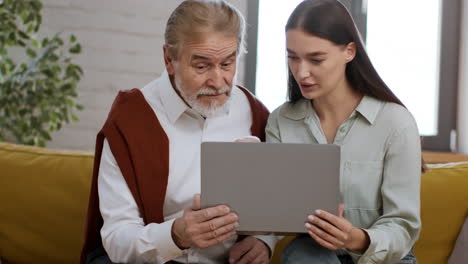 elderly man and young woman learning technology together on a couch