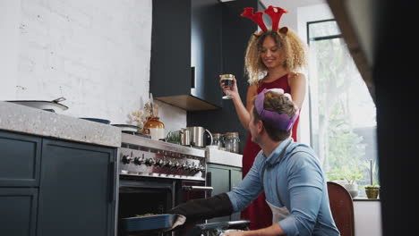 couple wearing fancy dress antlers and paper hat at home cooking vegetarian dinner on christmas day