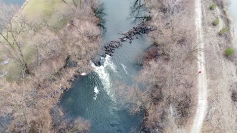 pequeña presa de río y rápidos en el pintoresco, idílico, árbol de sauce bordeado río en invierno con una persona vestida de rojo corriendo en la pista en el campo rural de boise, idaho, ee.uu.