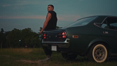 man leaning on a vintage car at dusk