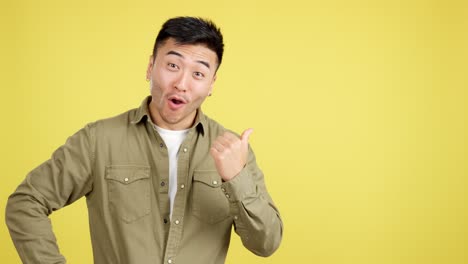 asian man expressing surprise and pointing on yellow background