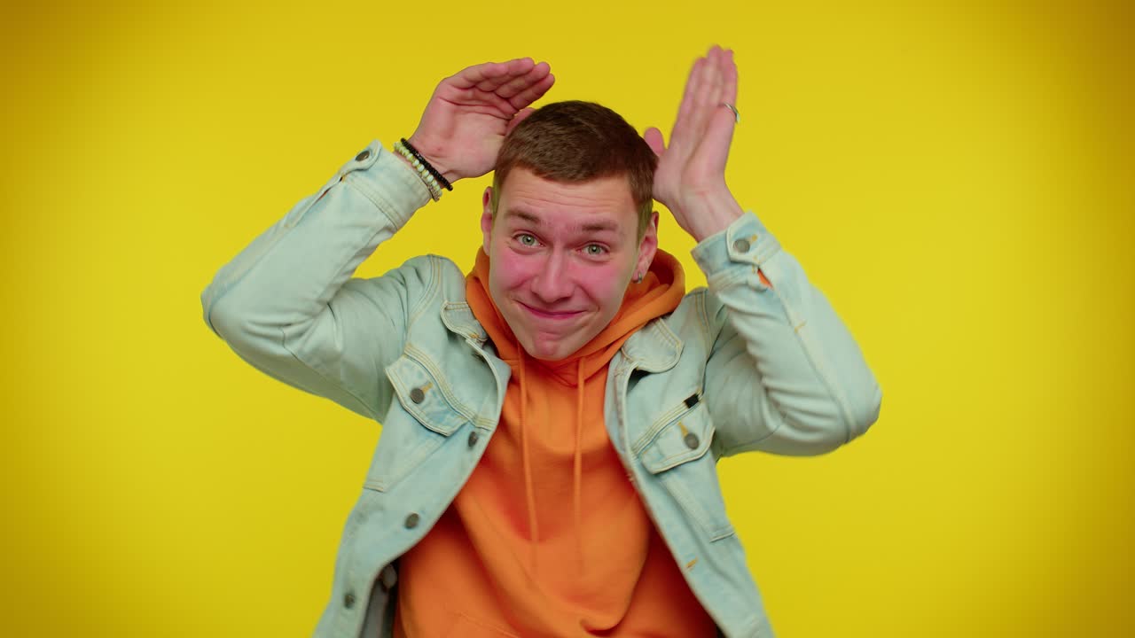 사랑스러운 재미있는 남자가 우호적으로 미소 짓고, 머리에 토끼 귀의 제스처를 하고, 재미있고, 우스스러운 기분을 가지고 있습니다.