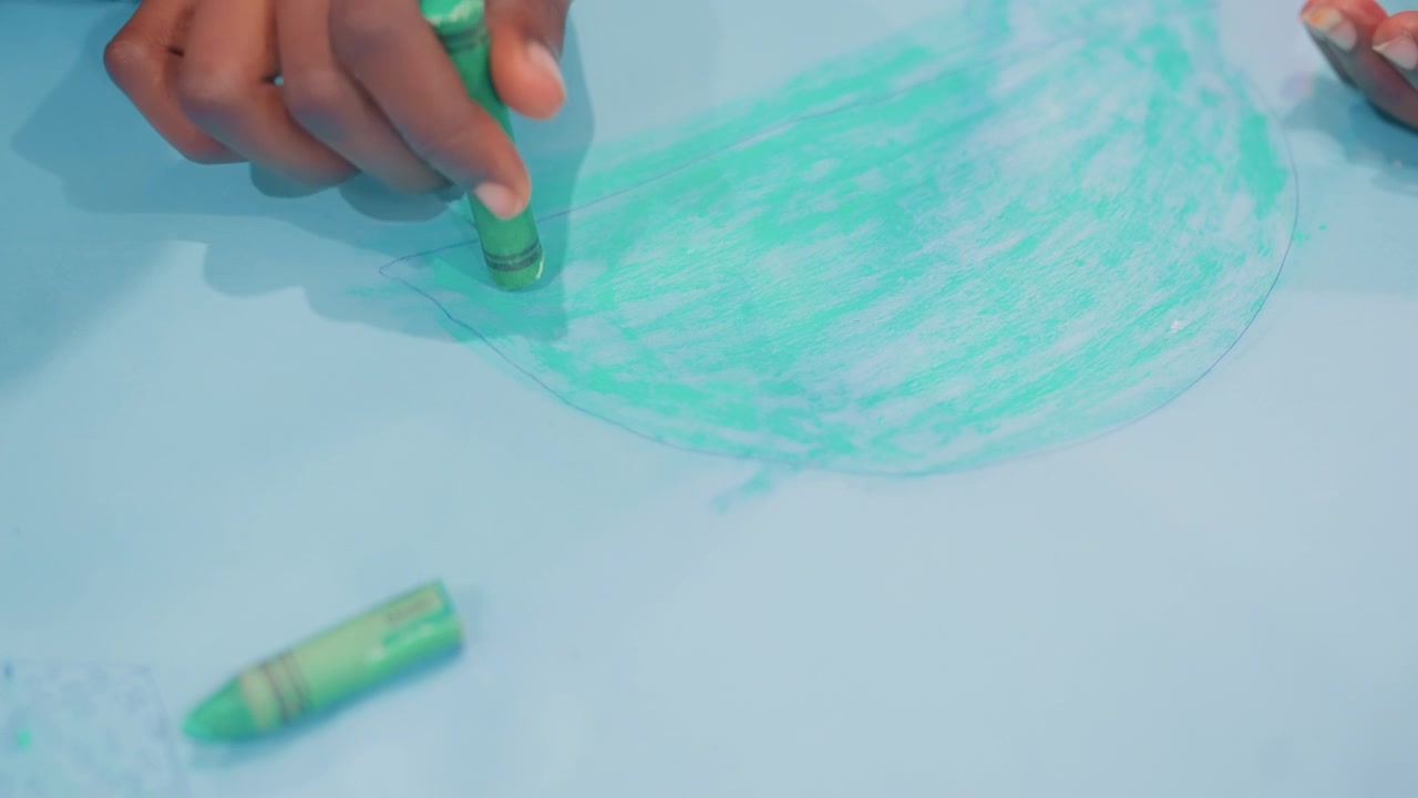 Closeup child hand shading with green crayon on blue paper, bold circular scribble, crayon stub nearby, playful exploration, nurturing presence, bright textured strokes, parentchild bonding moment