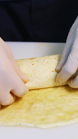 cooking meat and cheese pita with vegetables. hands in latex gloves roll up a pita roll. concept video. vertical video