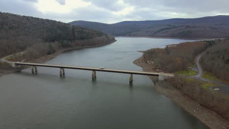 drone tracking a truck over a mountain bridge that crosses a mountain lake in late autumn or early winter