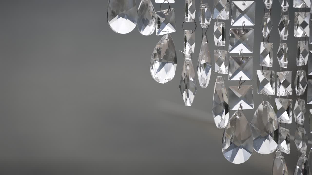 Close-up of crystal chandelier pendants hanging against a soft gray background. The faceted glass pieces catch and reflect light, creating a luxurious and elegant atmosphere.