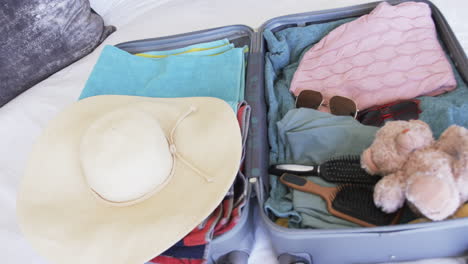 a suitcase is open, revealing neatly packed clothes and a teddy bear