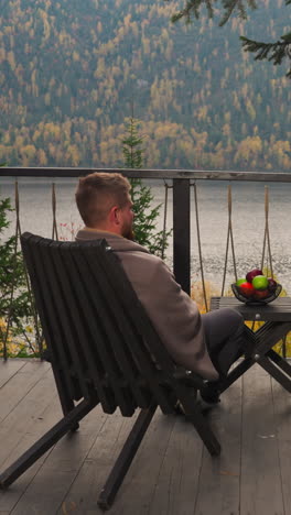 woman and man on terrace sit at table with fruits. friends enjoy time together on balcony against river and mountains. ideal autumn time-spending