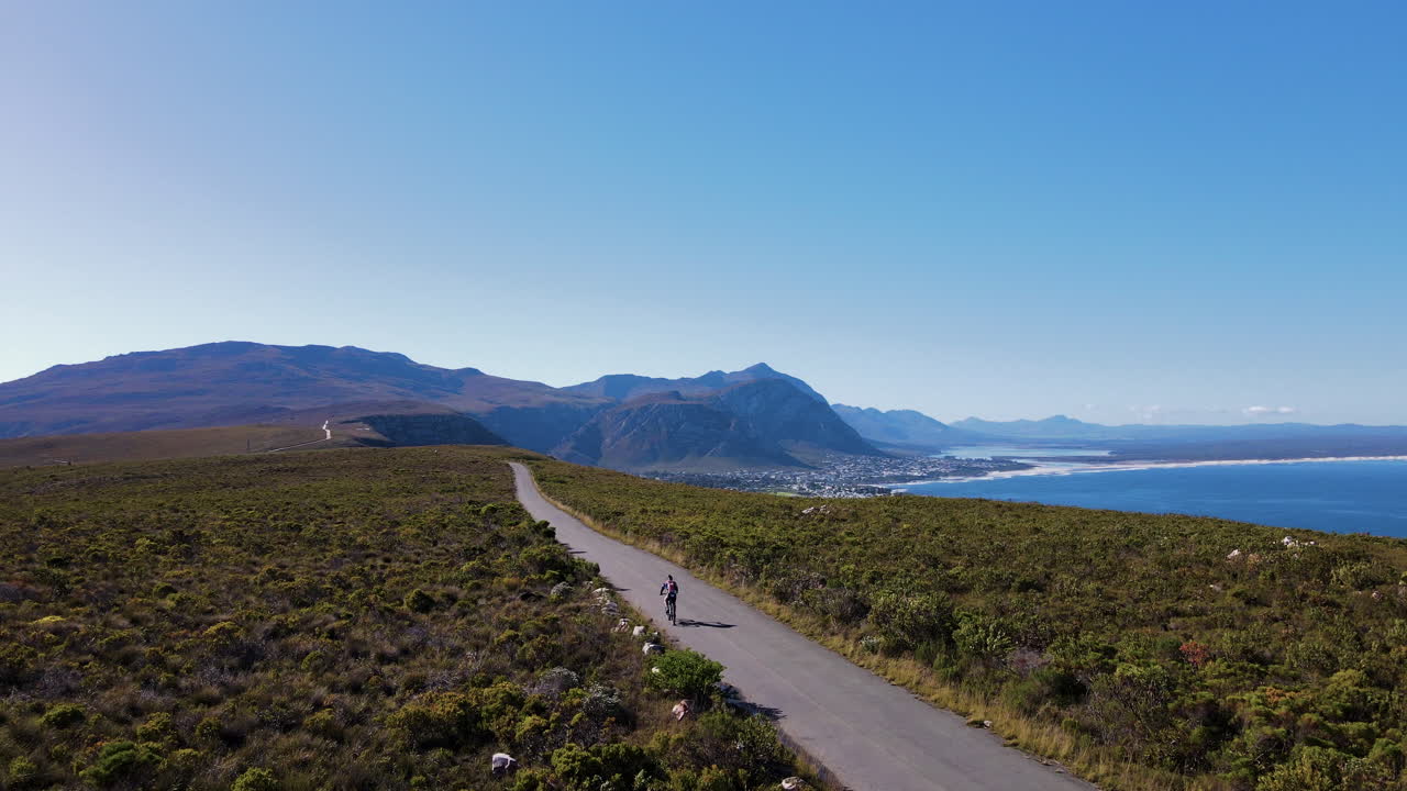 ciclista en una pintoresca carretera de montaña entre los fynbos con vistas épicas al océano, hermanus