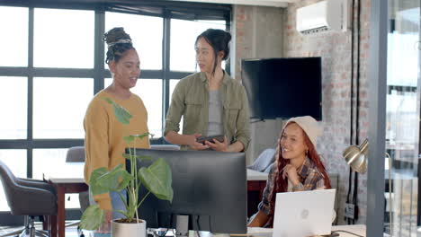 diverse female team collaborating on project in modern office, using laptop and tablet