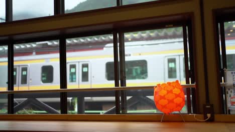 Vista-Del-Tren-Japonés-Mientras-Frena-Hasta-Detenerse-Desde-La-Ventana-De-Una-Cafetería-Al-Otro-Lado-De-La-Estación.