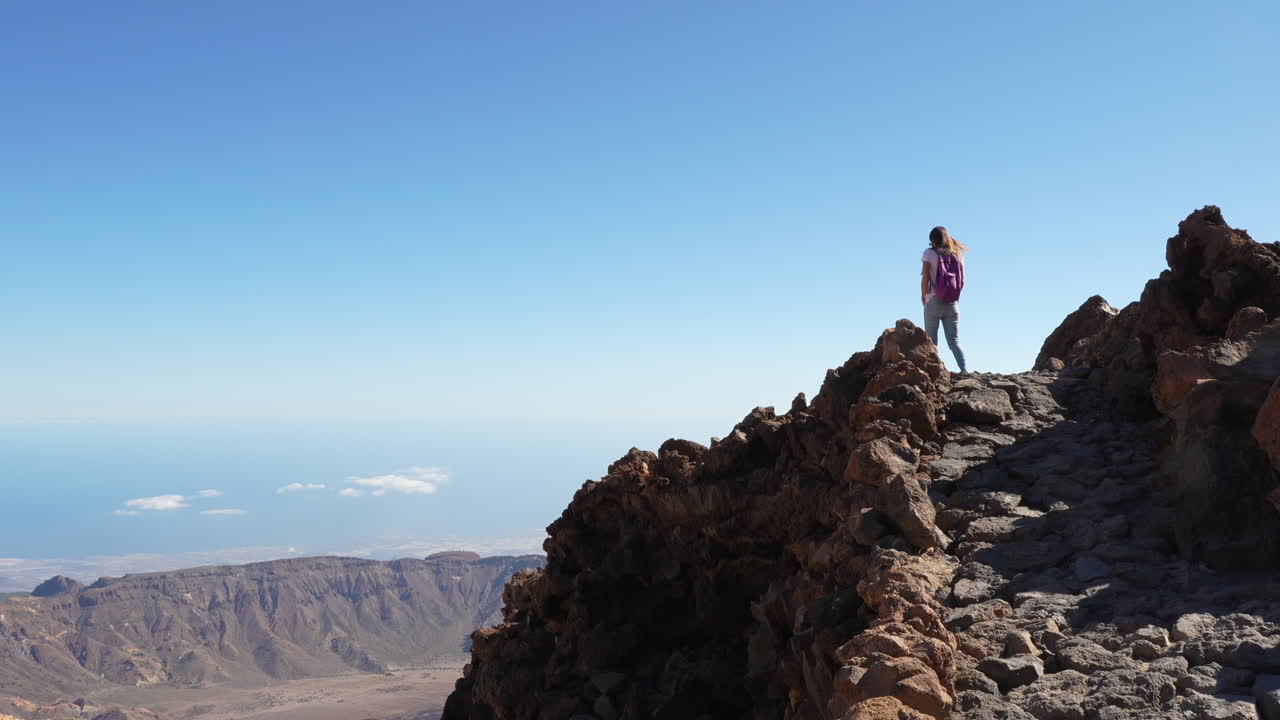 Woman with a backpack hiking on a rocky mountain path on a sunny day in the Canary Islands